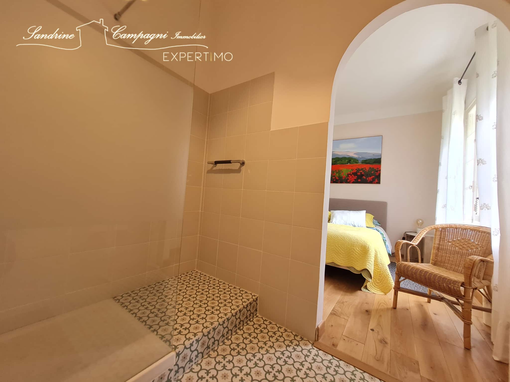 Salle de bain rénovée avec douche et chambre à coucher visible en arrière-plan.