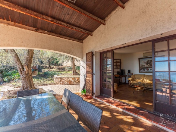 Terrace of a Provençal villa with sea view in La Turbie, outdoor furniture and trees.