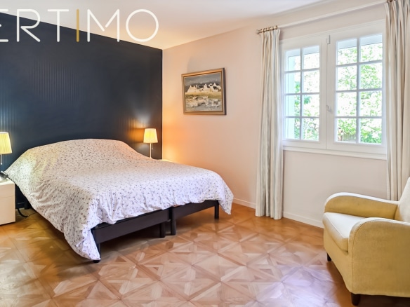 Room in a family property with double bed and armchair, light walls and bright windows.