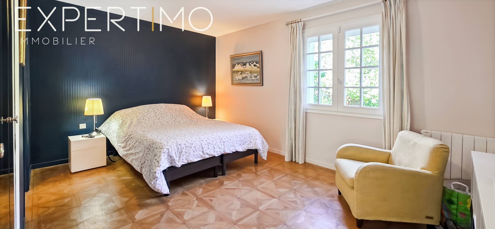 Room in a family property with double bed and armchair, light walls and bright windows.
