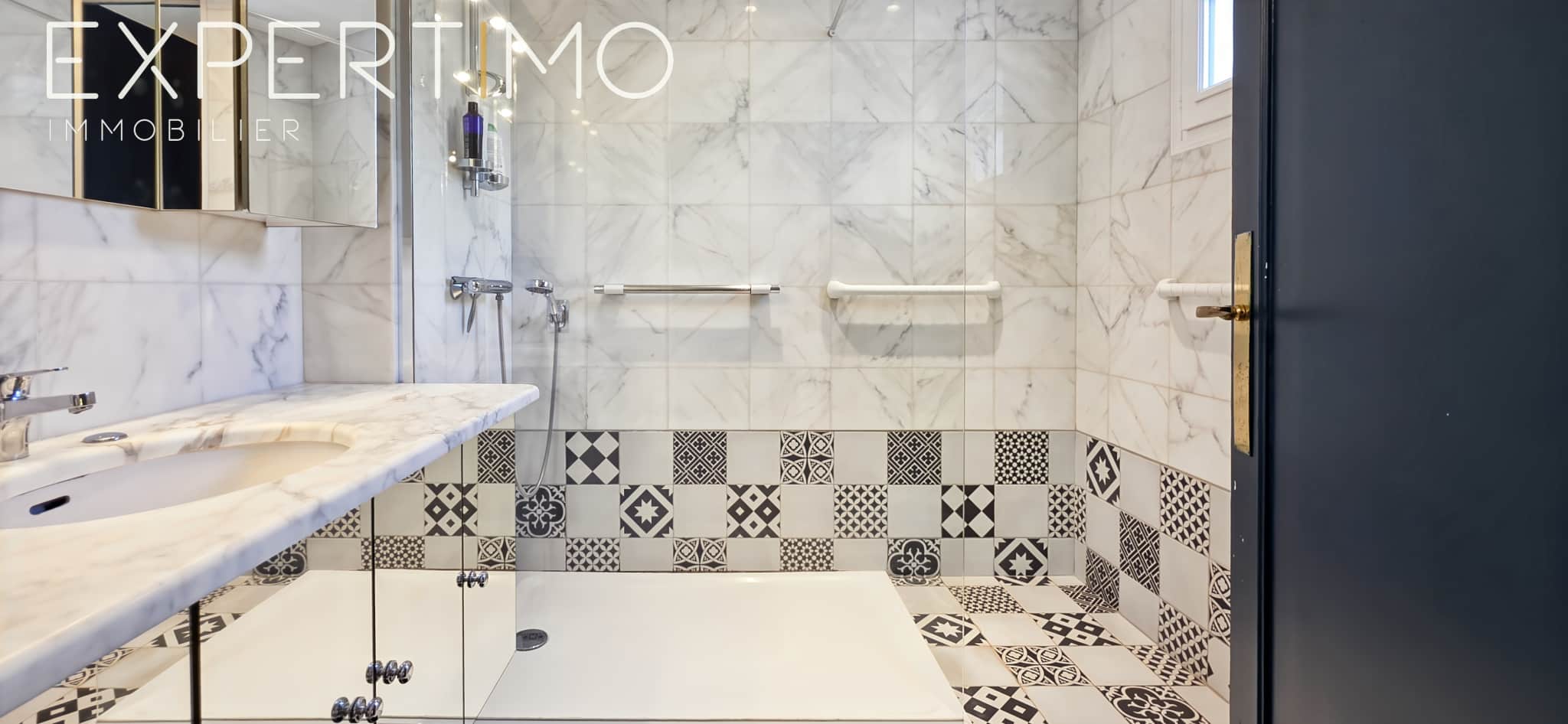 Modern bathroom with black and white tiles, walk-in shower and marble sink.