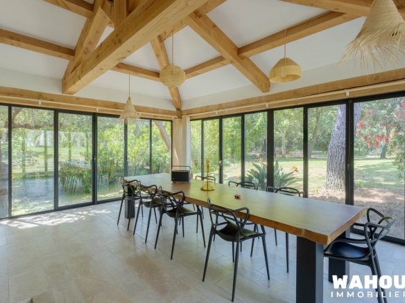 Intérieur d'une villa avec une grande table à manger et des fenêtres donnant sur un jardin verdoyant.