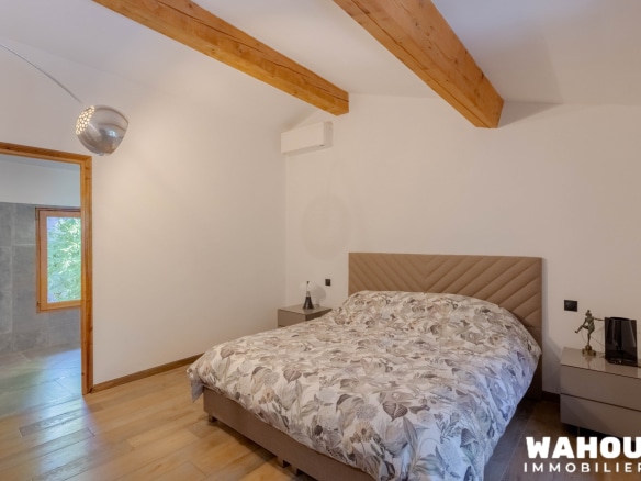 Chambre d'une villa avec lit double et décoration sobre, lumière naturelle et poutres en bois apparentes.