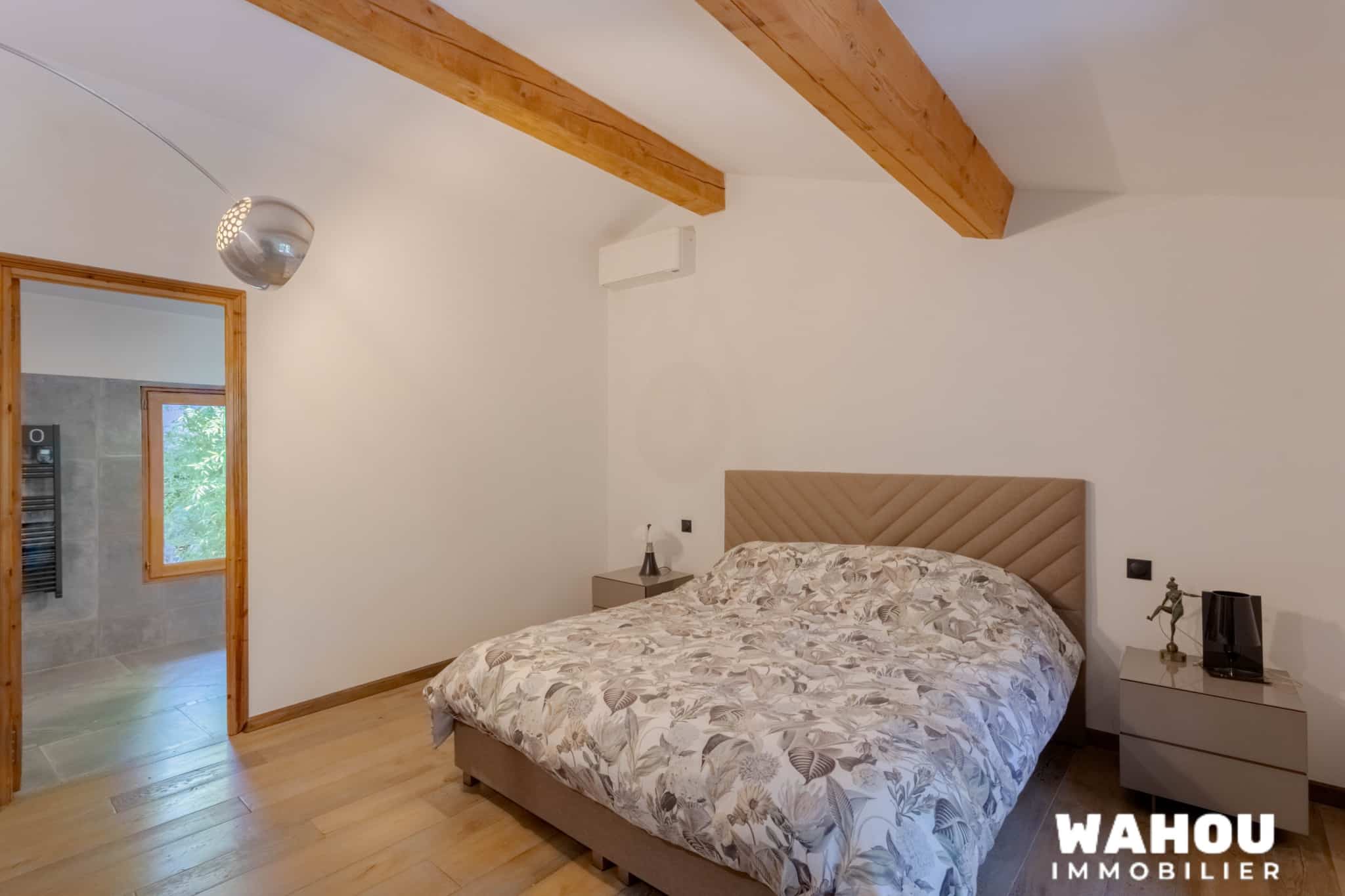 Chambre d'une villa avec lit double et décoration sobre, lumière naturelle et poutres en bois apparentes.