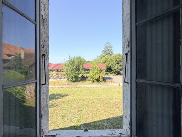 Vue depuis une fenêtre ouverte sur un terrain avec une grange en arrière-plan à Ornex.