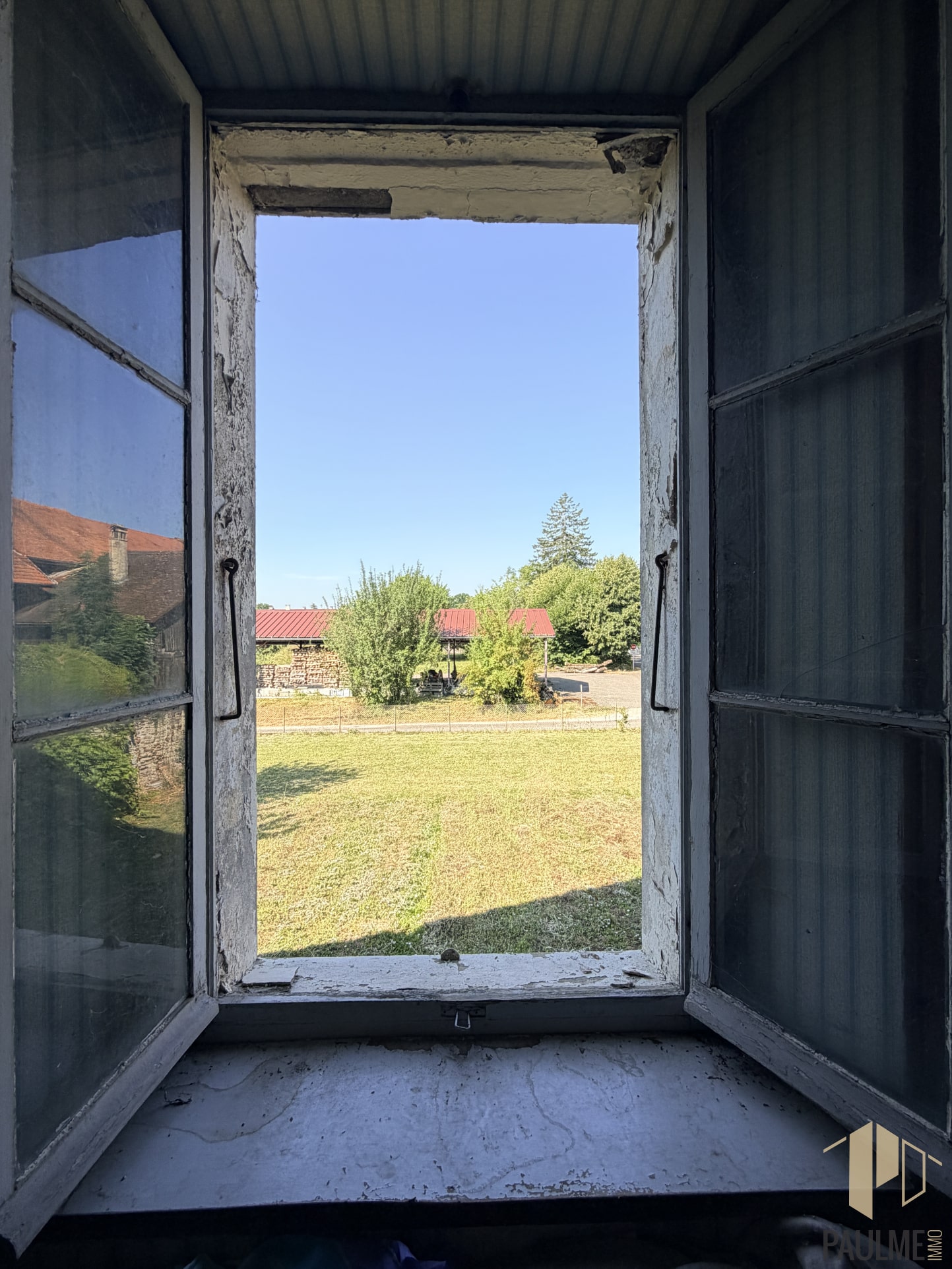 Vue depuis une fenêtre ouverte sur un terrain avec une grange en arrière-plan à Ornex.