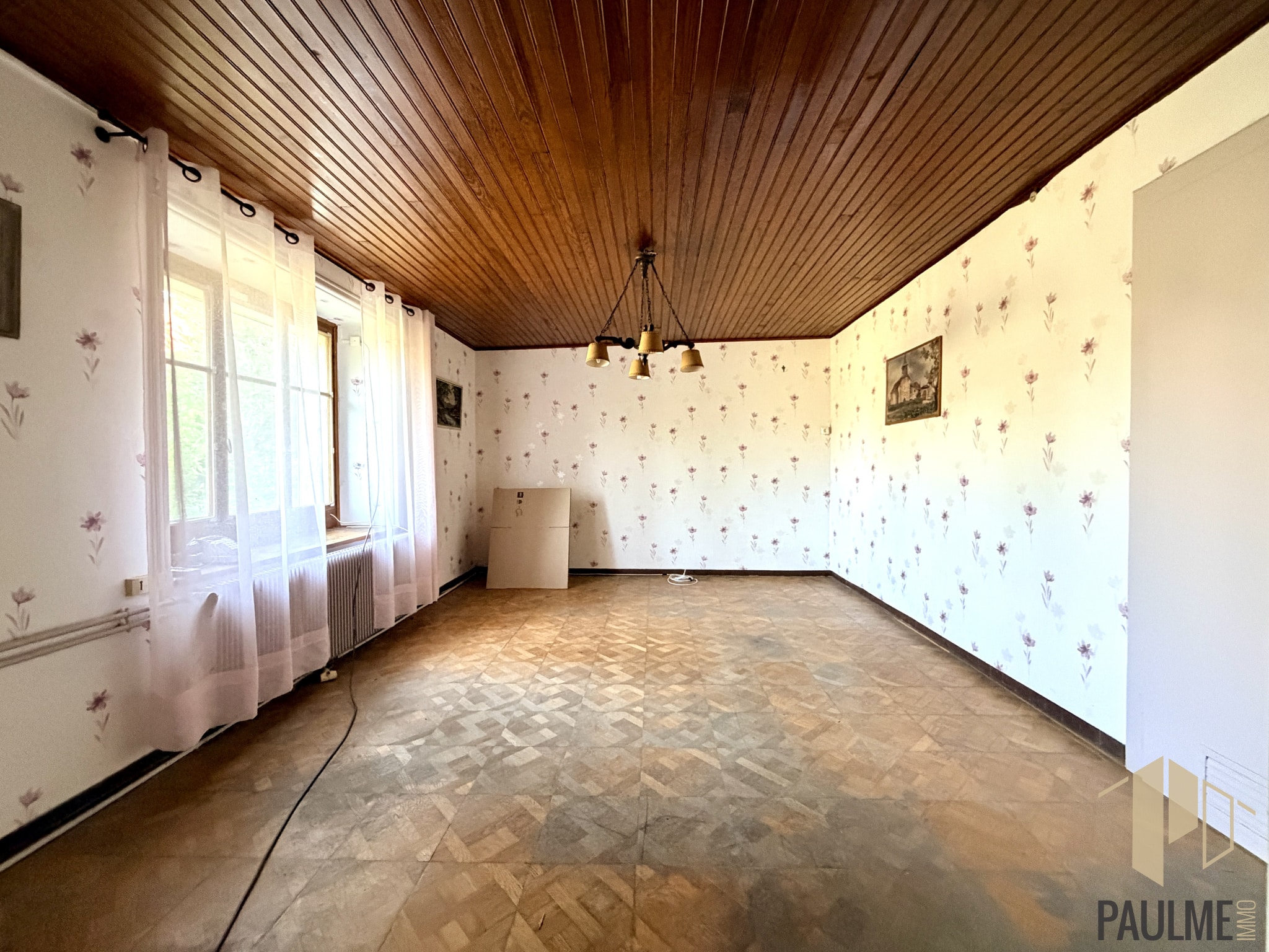 Intérieur d'une grange à rénover avec un sol en carreaux et des murs décorés de papier peint floral.