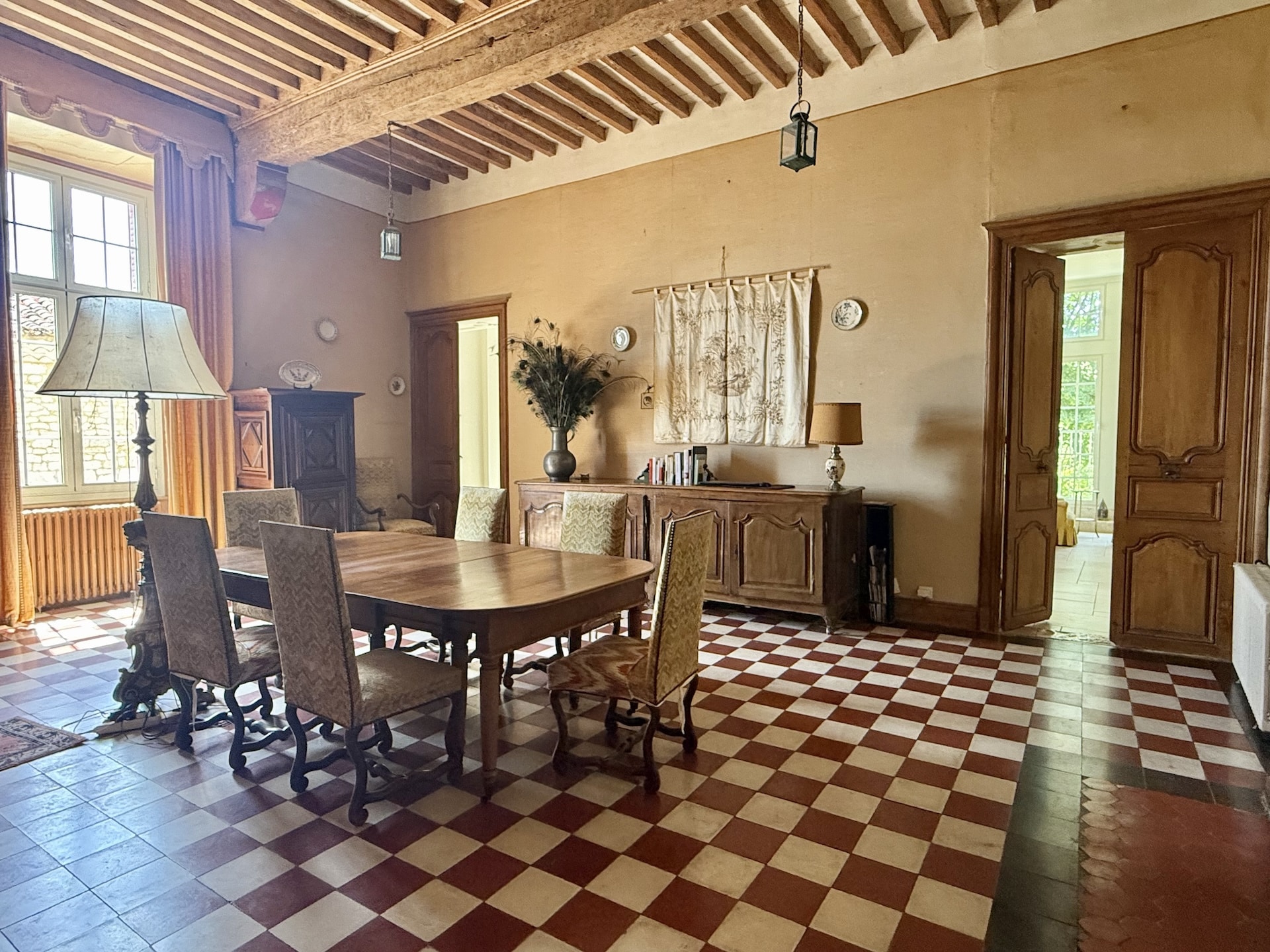 Intérieur d'une salle à manger avec table en bois et chaises, murs en pierre et sol en carreaux rouges et blancs.