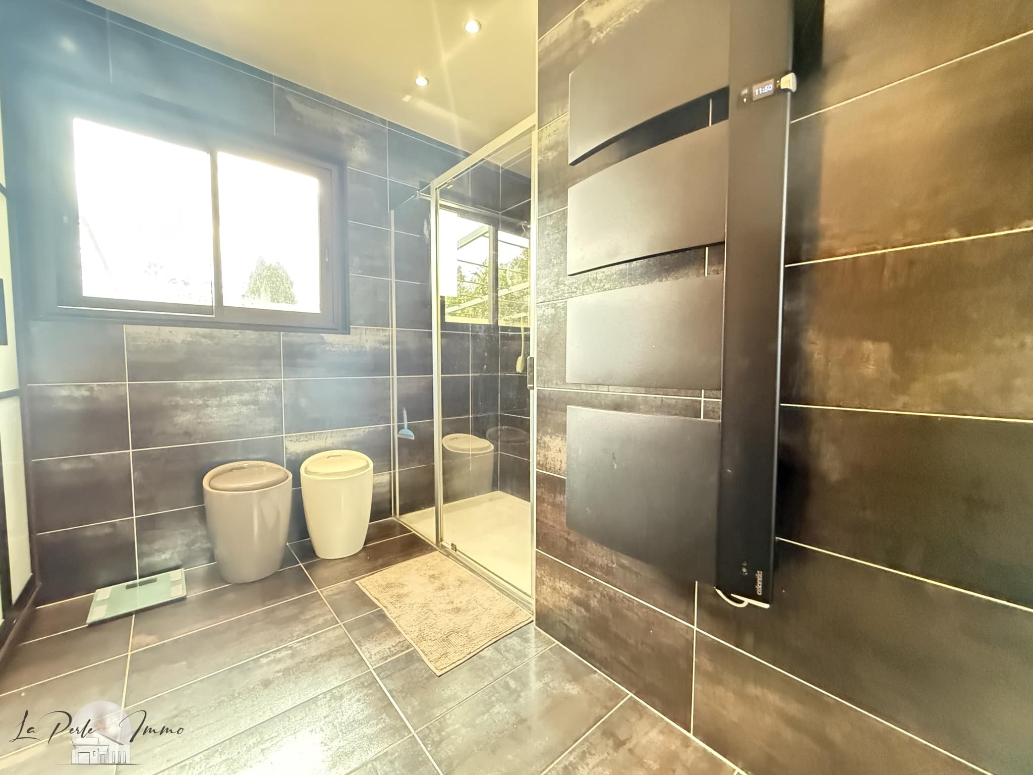 Salle de bain moderne avec douche, toilettes et carrelage foncé dans une villa à Perpignan.