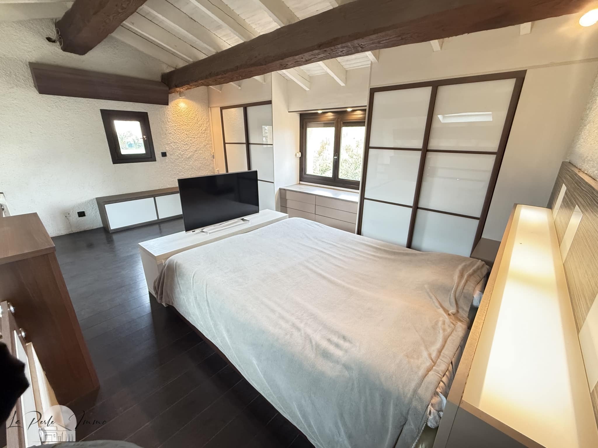 Chambre d'une villa avec lit et télévision, murs blancs et poutres apparentes