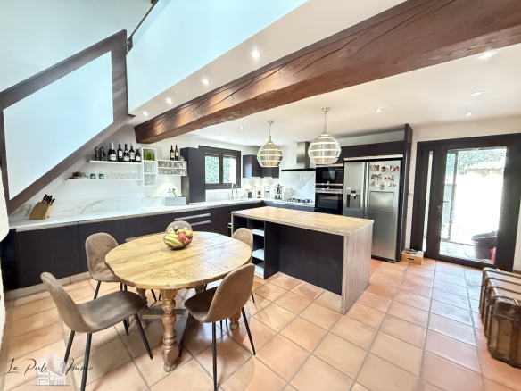 Intérieur d'une villa avec cuisine moderne et salle à manger, murs en pierre et lumière naturelle.