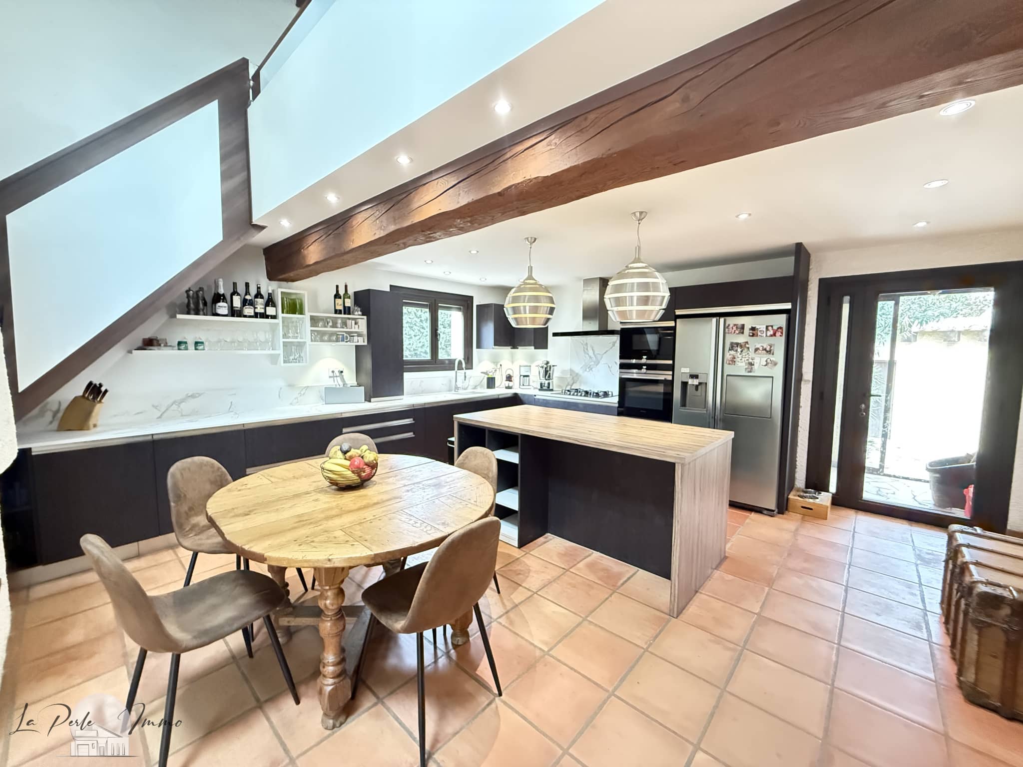 Intérieur d'une villa avec cuisine moderne et salle à manger, murs en pierre et lumière naturelle.