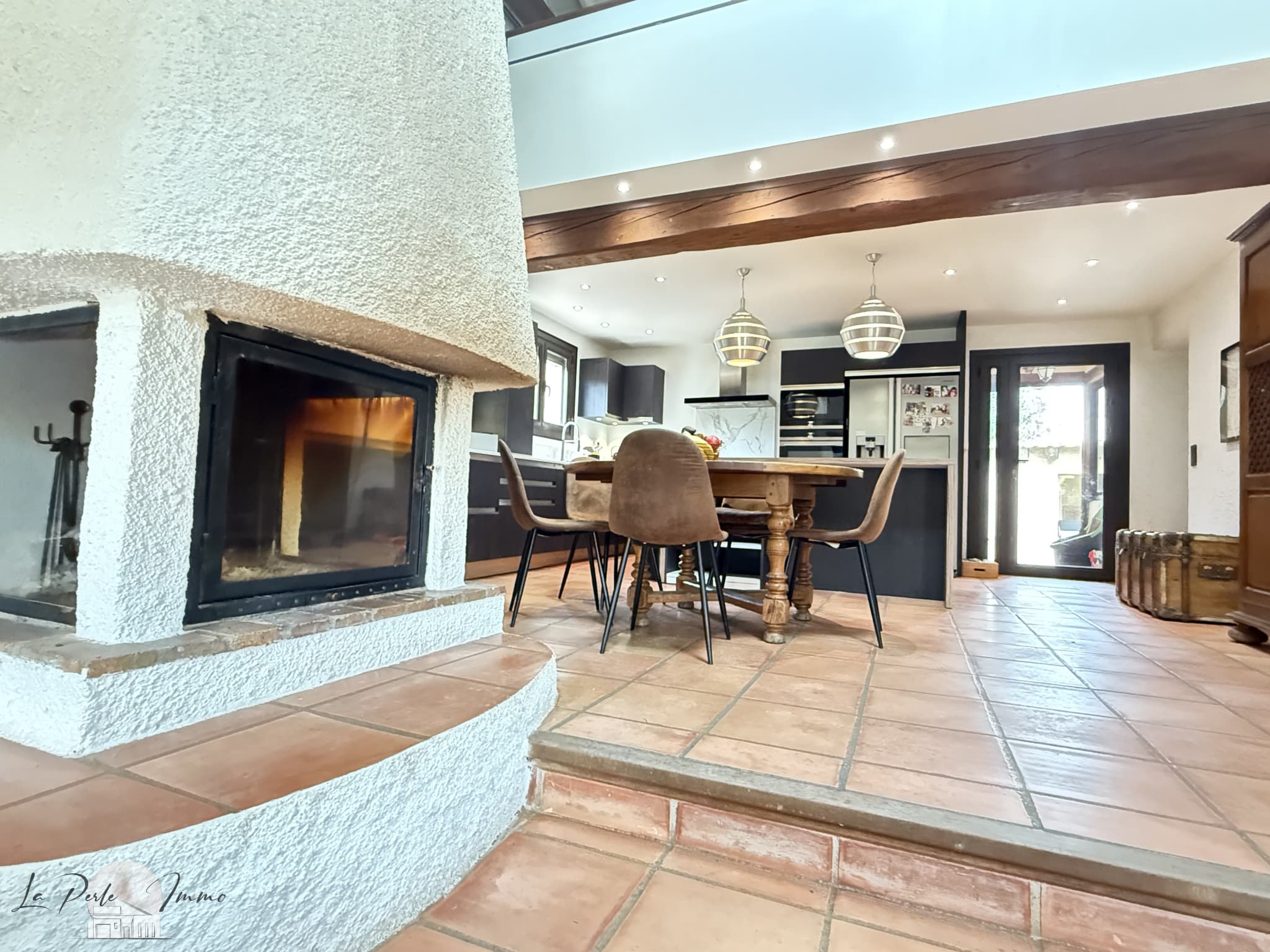 Intérieur d'une villa avec cheminée, table à manger et cuisine ouverte.
