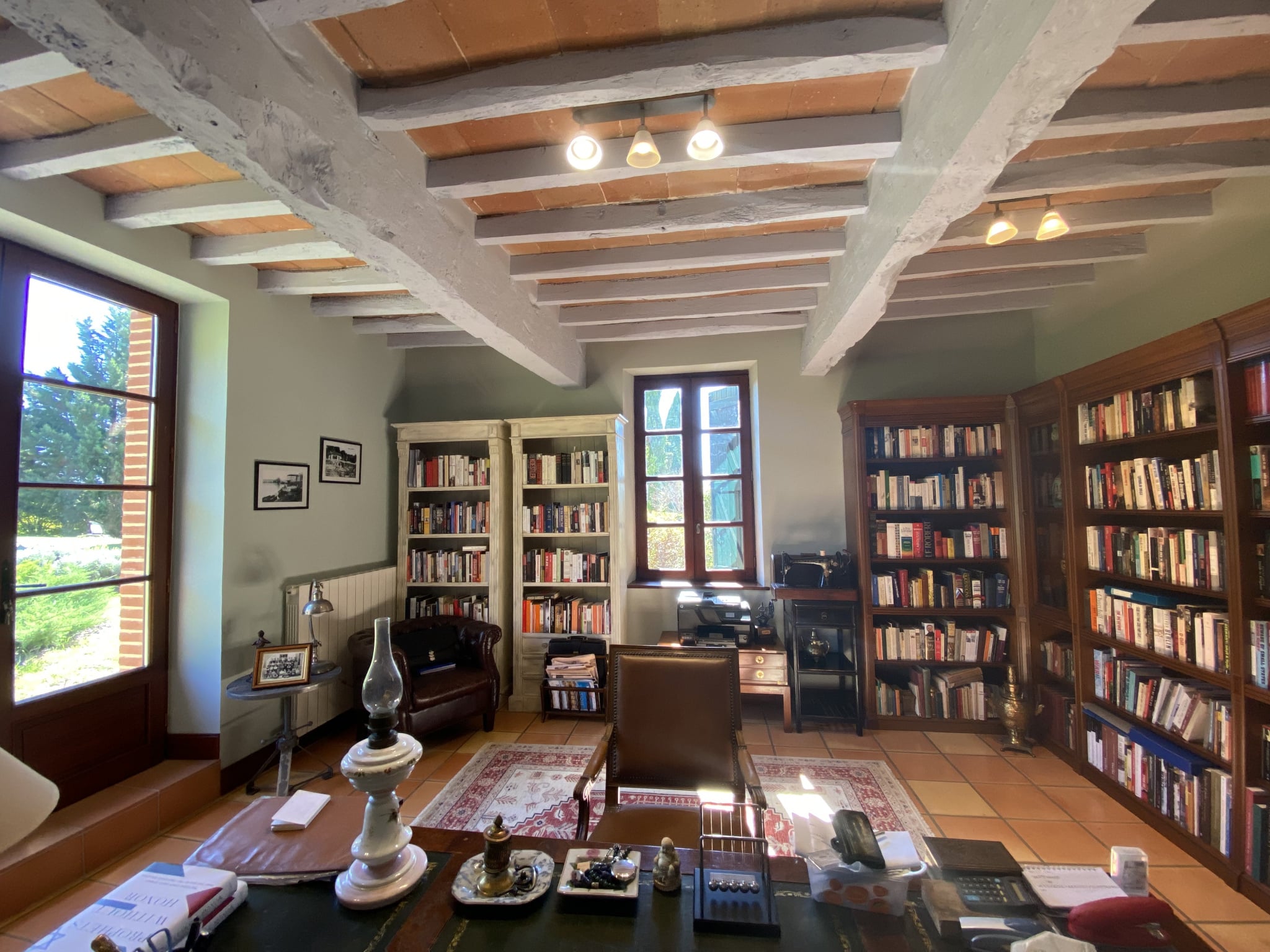 Interior of an office with bookshelves filled with books and a wooden desk, natural light
