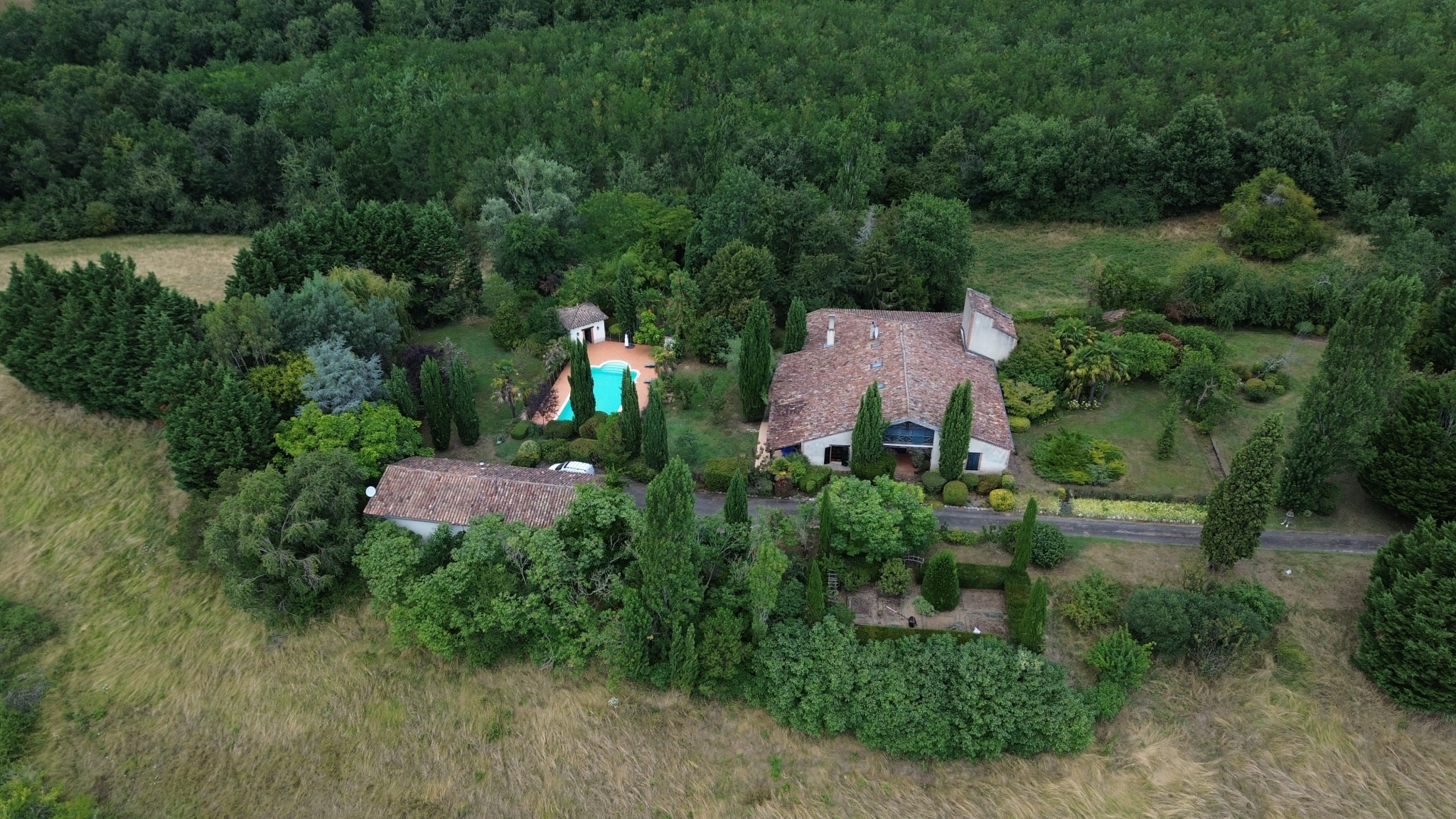 Aerial view of a country house with guest house and swimming pool, surrounded by gardens and hills.