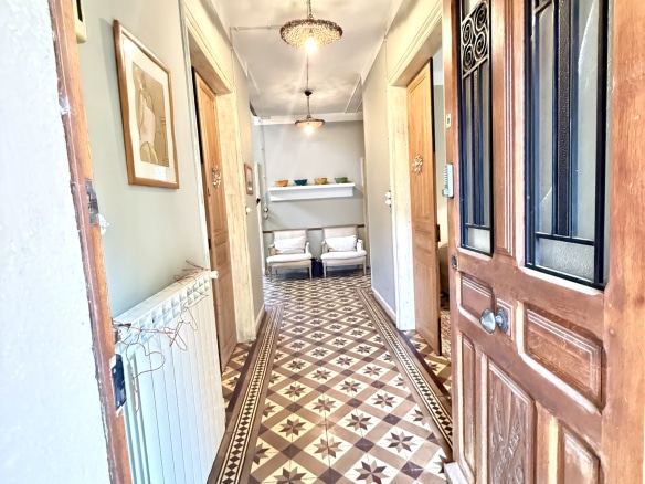 Intérieur d'une maison de maître avec un couloir décoré de carrelage ancien et des portes en bois.