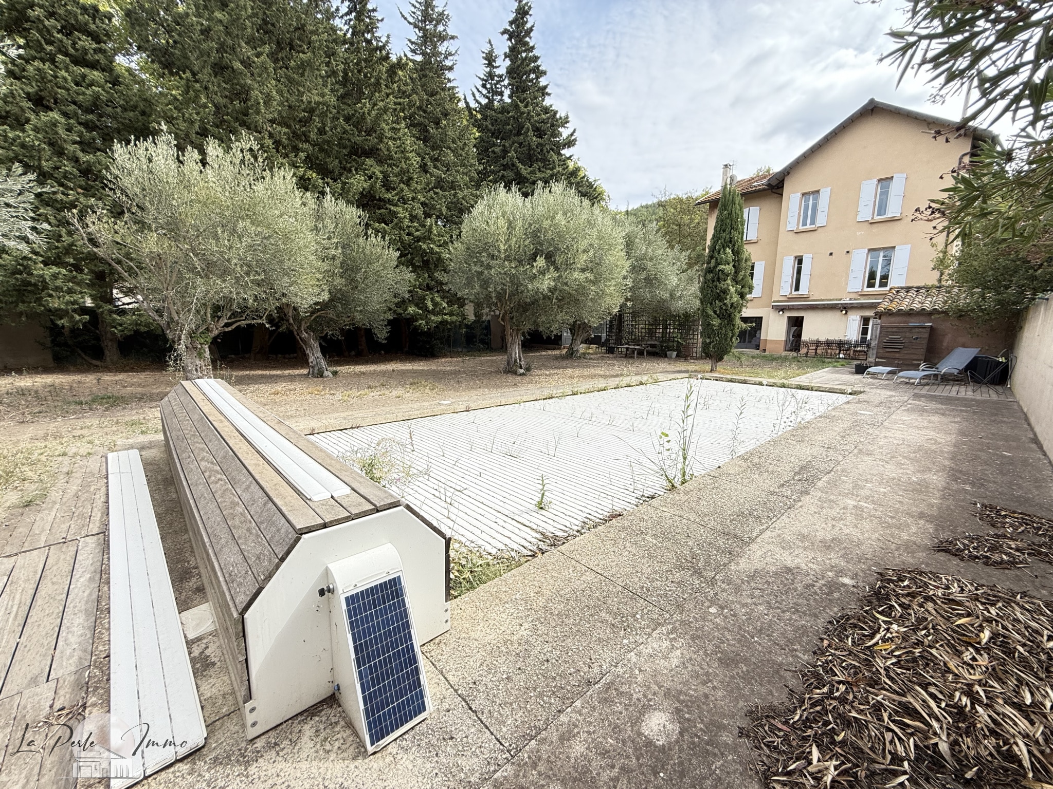 Jardin d’une maison de maître à Villeneuve-les-Corbières Vue du jardin d'une maison de maître avec piscine vide et arbres.