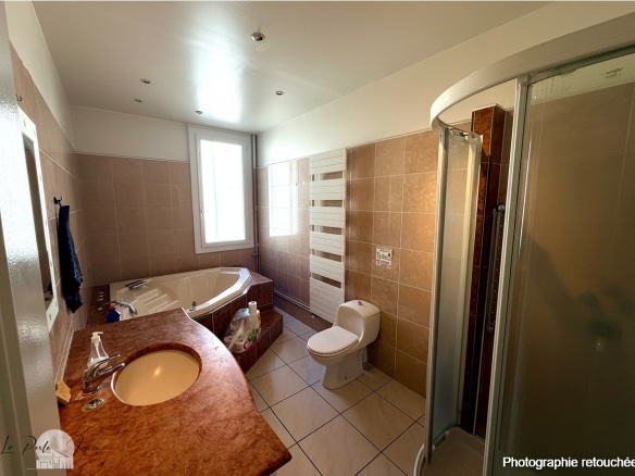 Salle de bain spacieuse avec baignoire et douche, carrelage clair.
