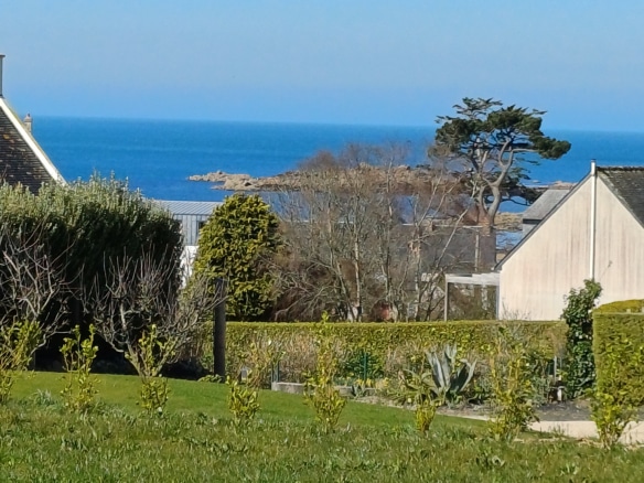 Sea view from a Breton stone house in Plougasnou, with a green garden in the foreground.