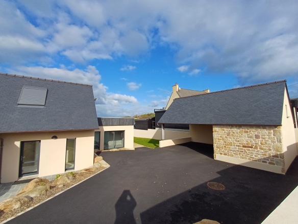 View of a fully renovated Breton stone house in Plougasnou, with an outdoor space and a cloudy sky.