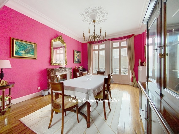 Intérieur d'une maison de maître avec murs roses, table à manger et mobilier ancien.