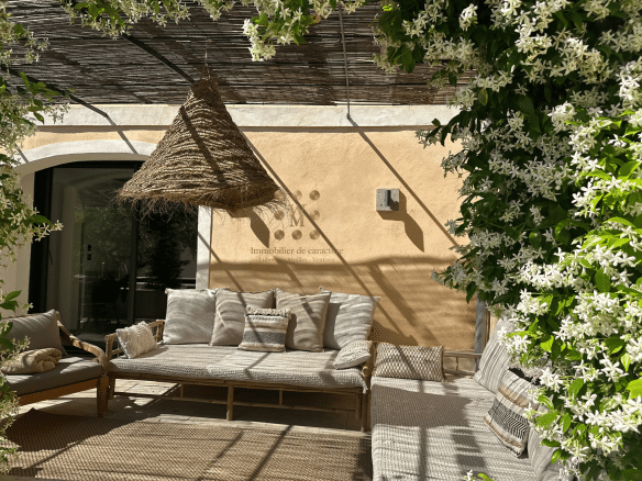 Terrasse d'une maison de village avec mobilier en bois et plantes fleuries.