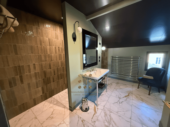Salle de bain moderne avec carrelage en marbre et lavabo sur meuble, lumière douce.