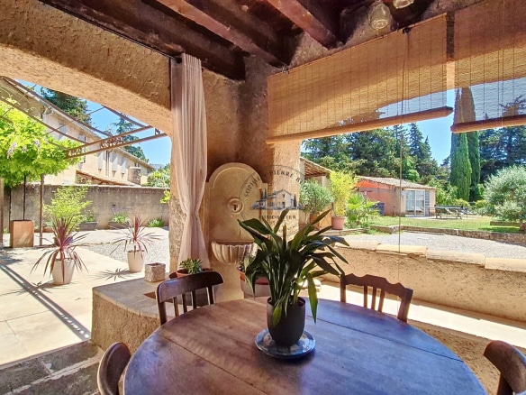 Terrace of an 18th century building with table and plants, overlooking garden and swimming pool.