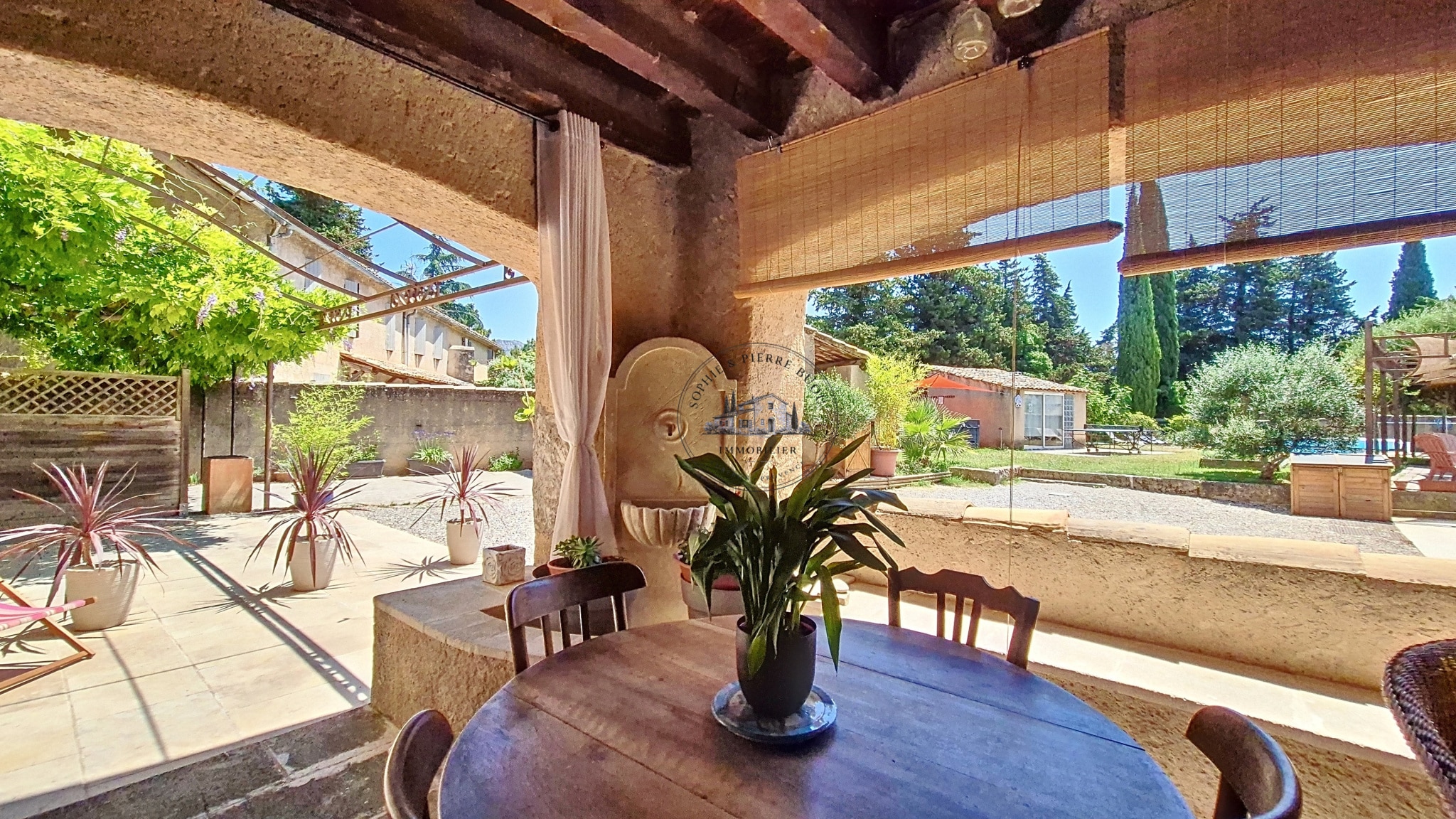 Terrace of an 18th century building with table and plants, overlooking garden and swimming pool.