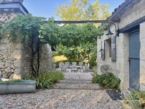 View of a stone complex with a courtyard and chairs, surrounded by greenery in Touffailles.