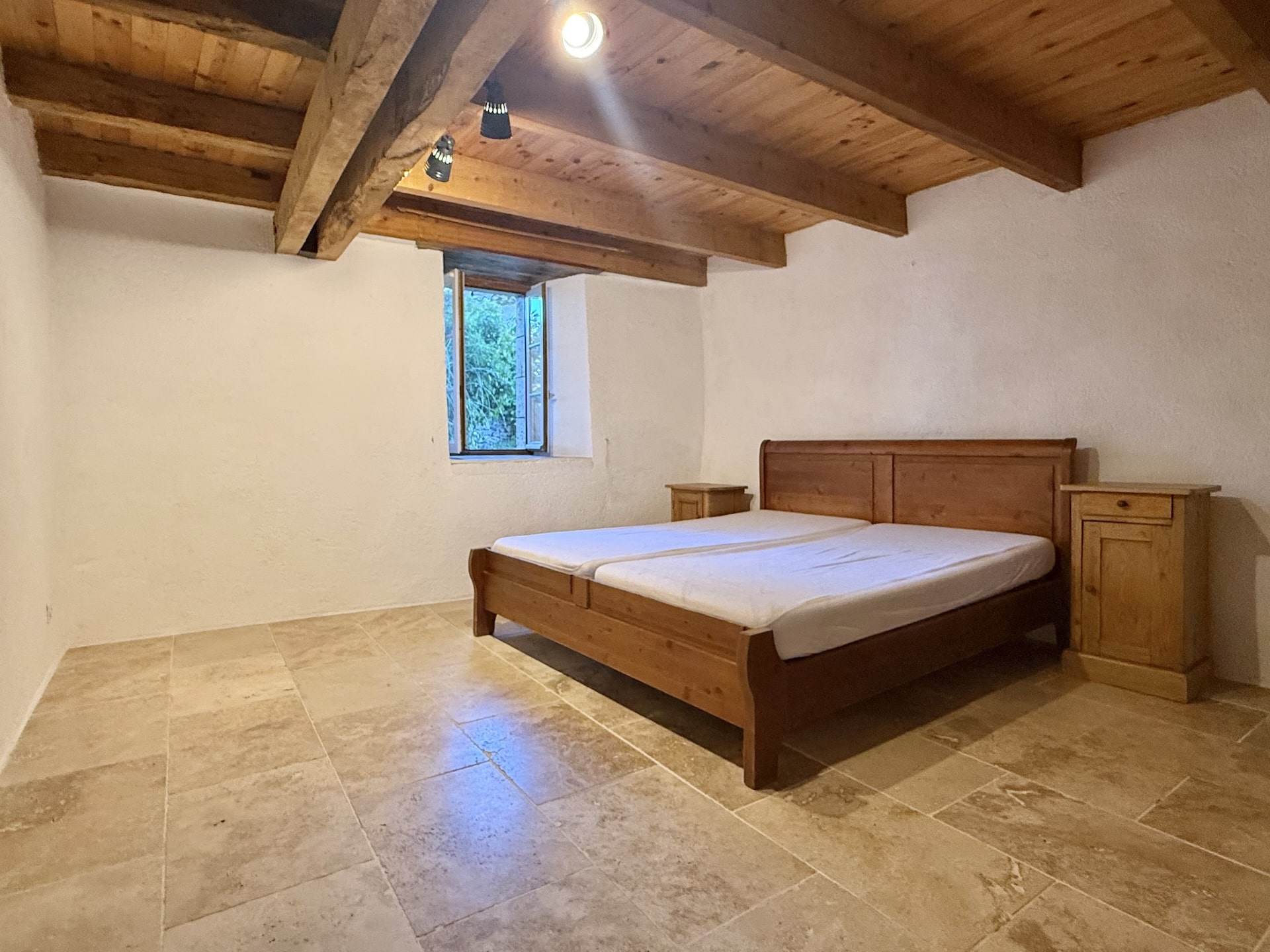 Room with wooden bed and stone walls, windows overlooking the outside.
