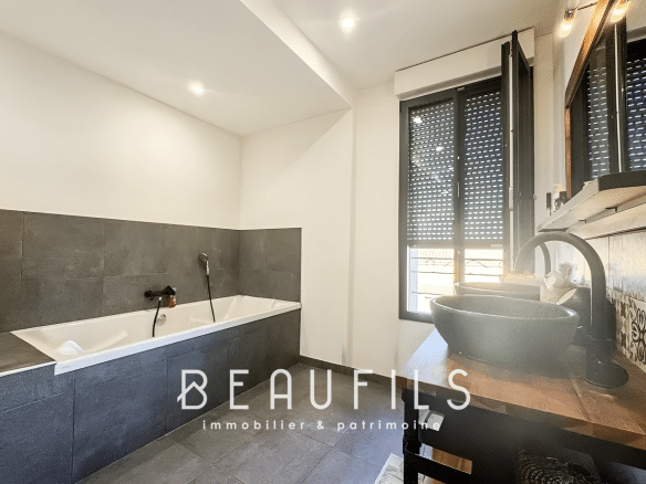 Modern bathroom with bathtub and sink, grey and black tiled walls.