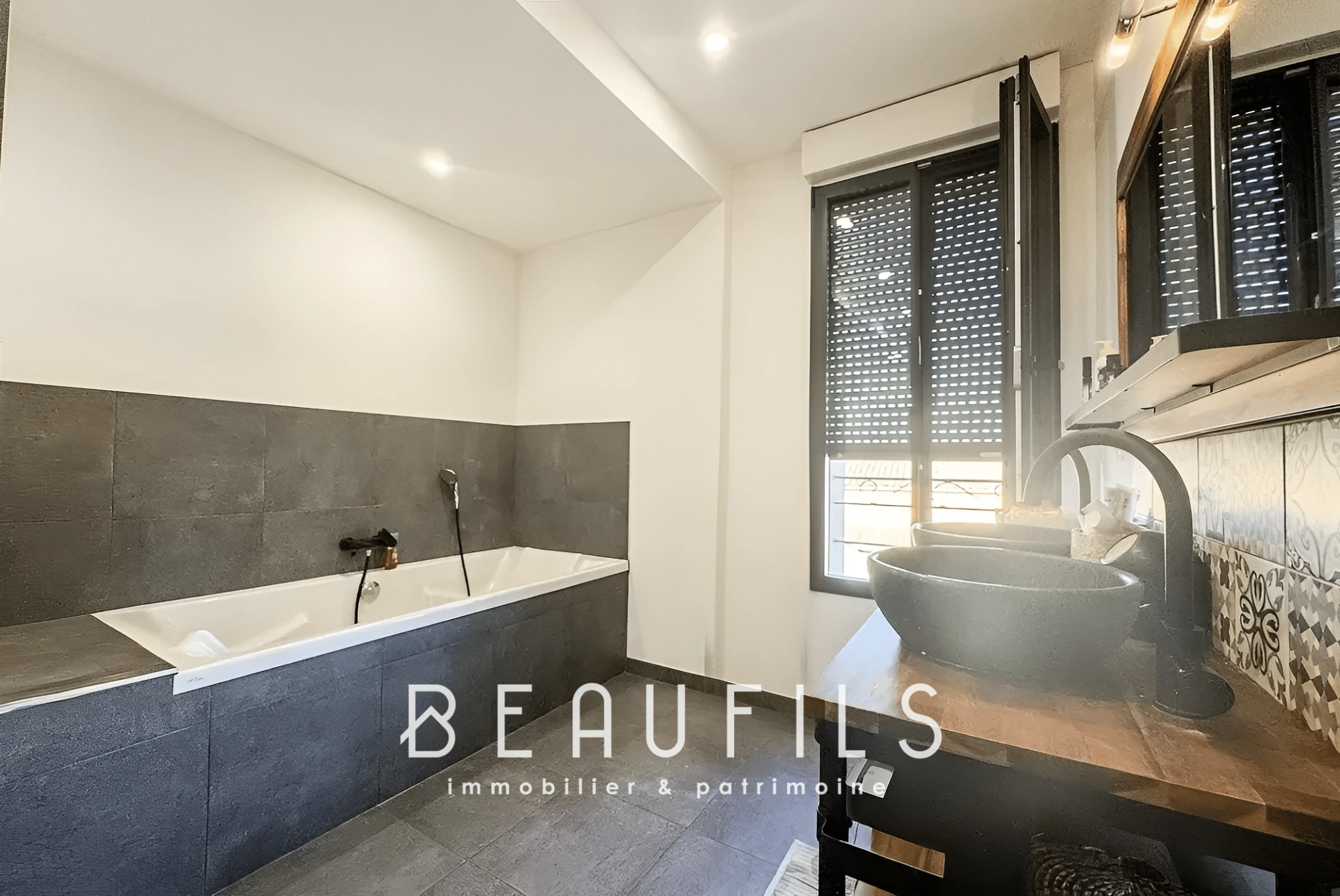 Modern bathroom with bathtub and sink, grey and black tiled walls.