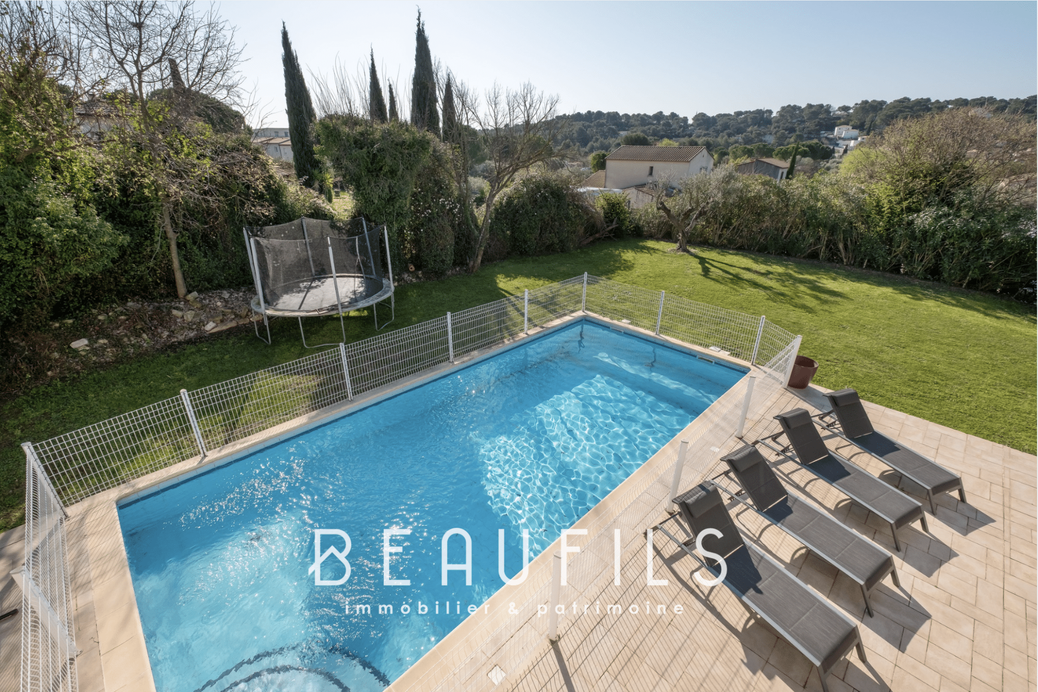 View of the swimming pool and garden of an architect-designed villa in Nîmes, with sun loungers and trampoline.
