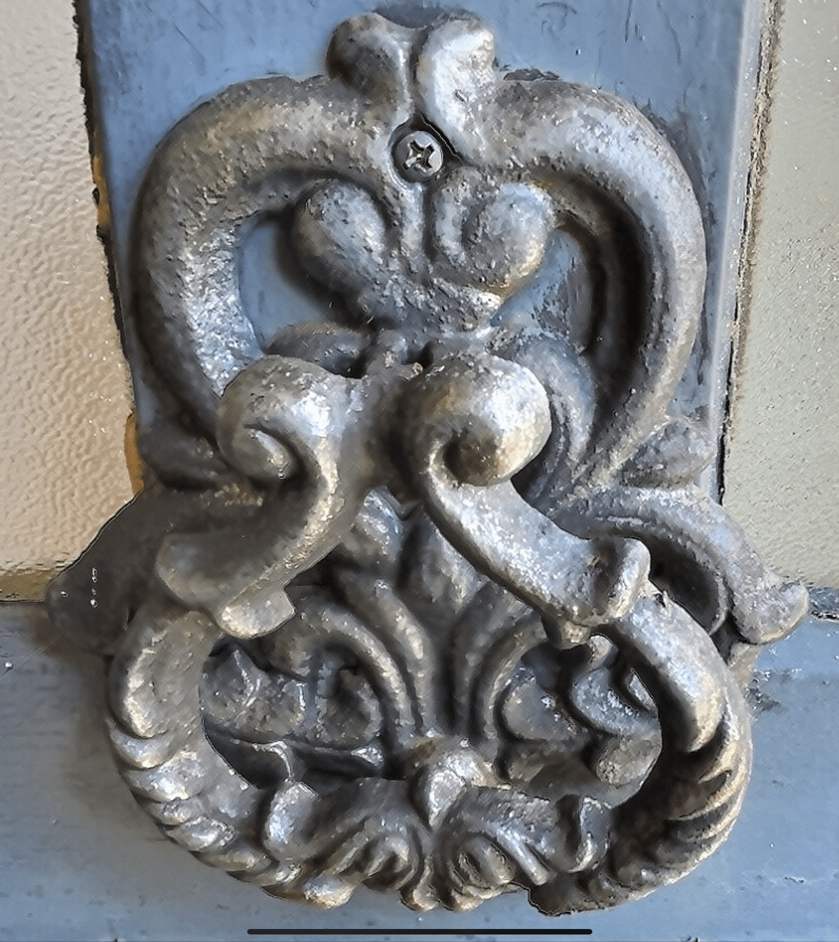 Poignée de porte en métal ornée, style XVIIIe siècle, sur un fond de bois.