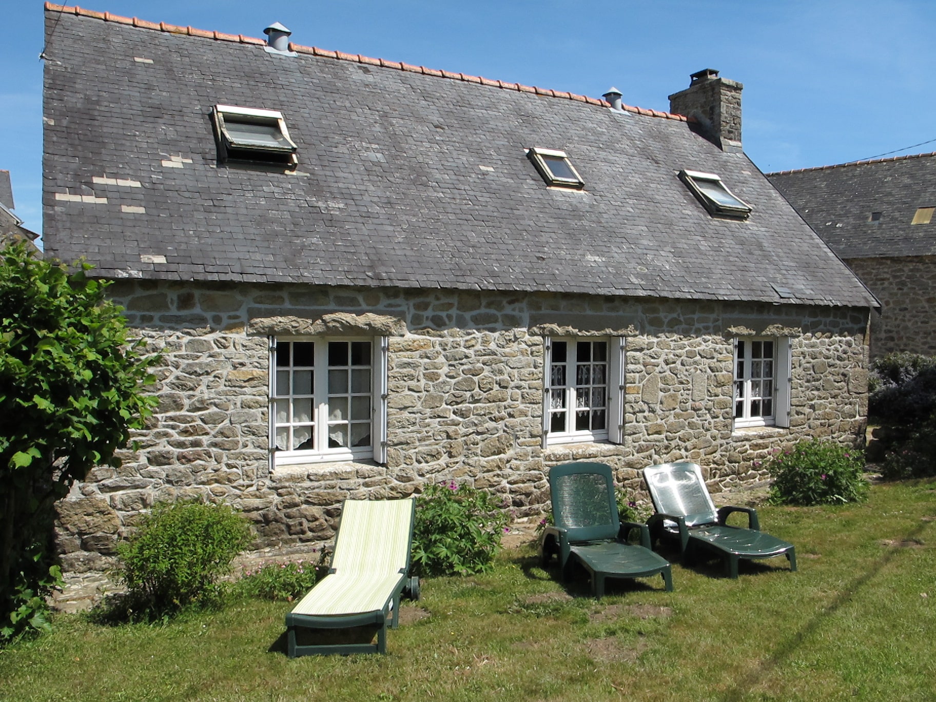 Corps de ferme en pierre avec chaises longues dans un jardin ensoleillé à Pont-l'Abbé.