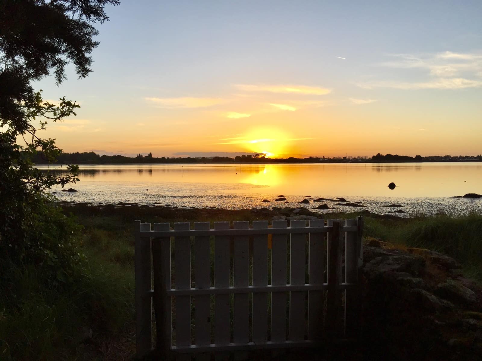 Coucher de soleil sur un plan d'eau avec une clôture en bois au premier plan, près de Pont-l'Abbé.