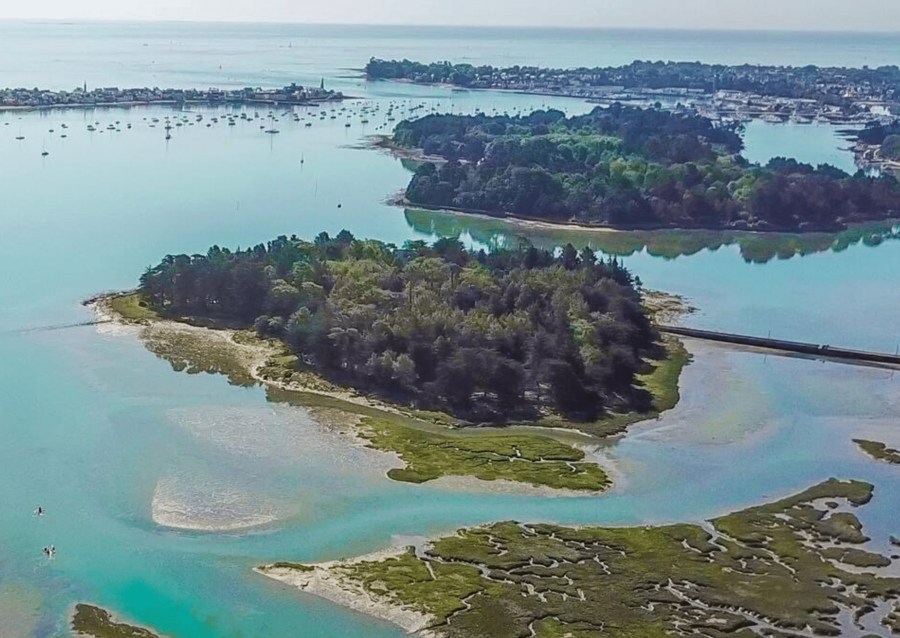 Vue aérienne d'une anse préservée entre terre et mer à Pont-l'Abbé, avec des îlots et des bateaux au loin.