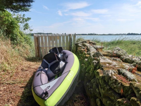 Un canoë sur la rive près d'une clôture en bois, avec une vue sur l'eau et la végétation environnante.