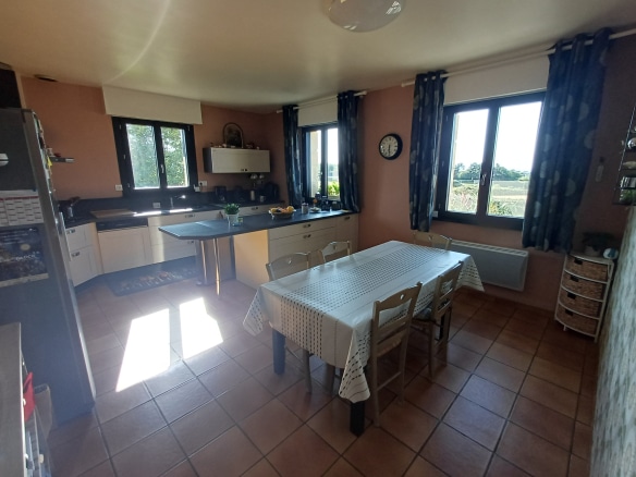 Spacious kitchen with dining table and windows overlooking the outside.