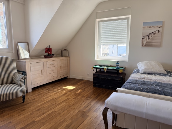 Chambre lumineuse avec un lit simple, un meuble en bois et un fauteuil à rayures.