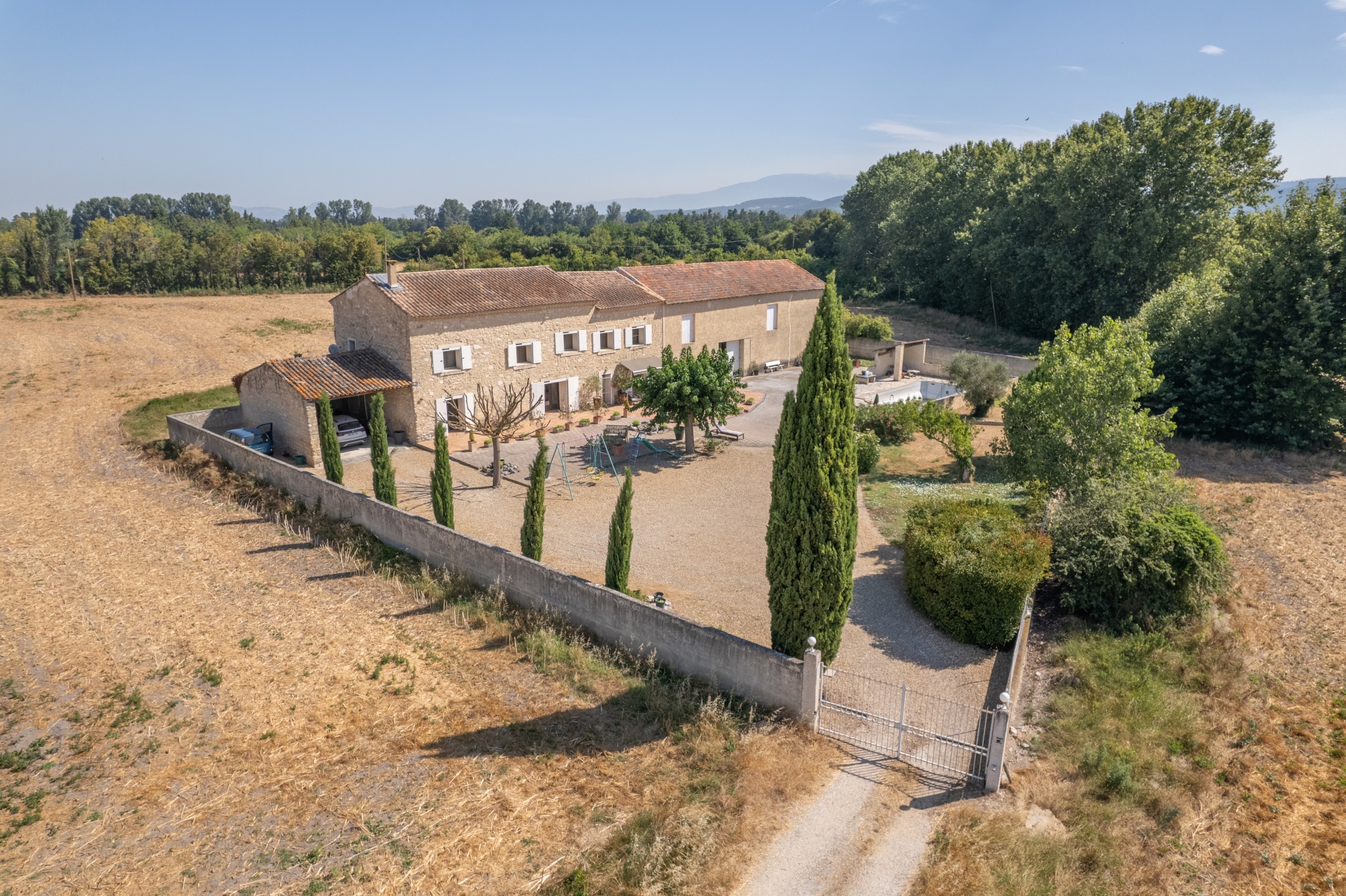 Vue aérienne d'un mas en pierre entouré de champs et d'arbres, situé près de L'Isle-sur-la-Sorgue.