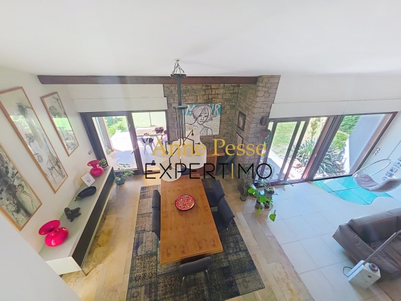 Interior of a modern villa with a large wooden table and bay windows overlooking the garden.