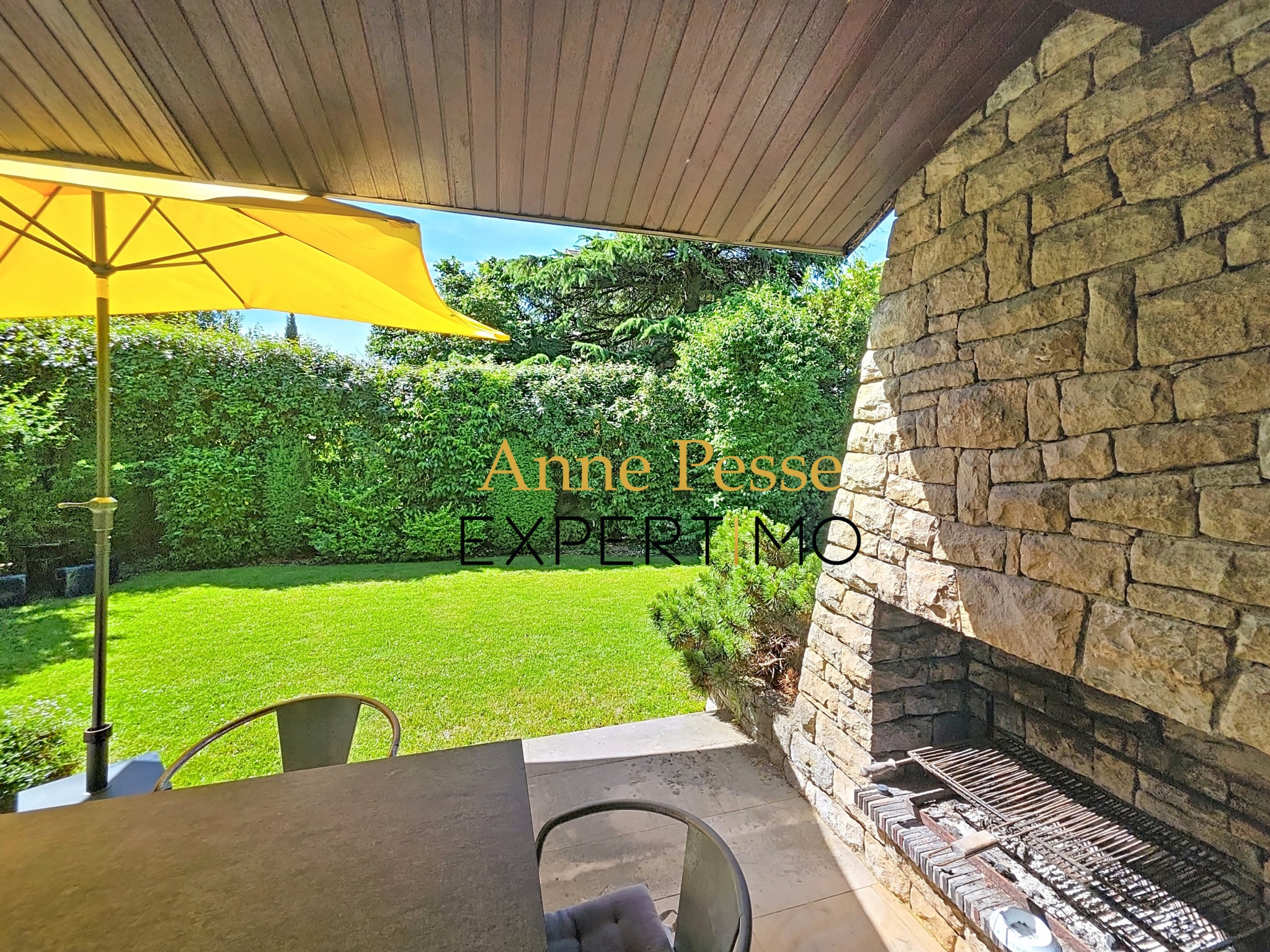 Terrace of an architect-designed villa with a yellow parasol and a barbecue area, green garden in the background.