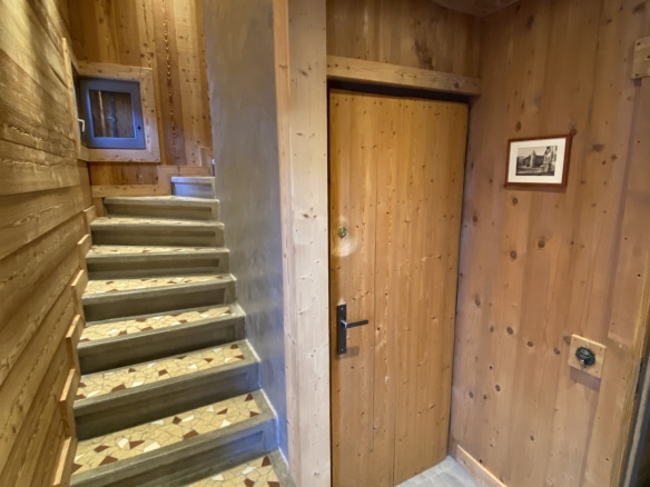 Entrance to a renovated apartment with wooden stairs and wooden door, chalet style.