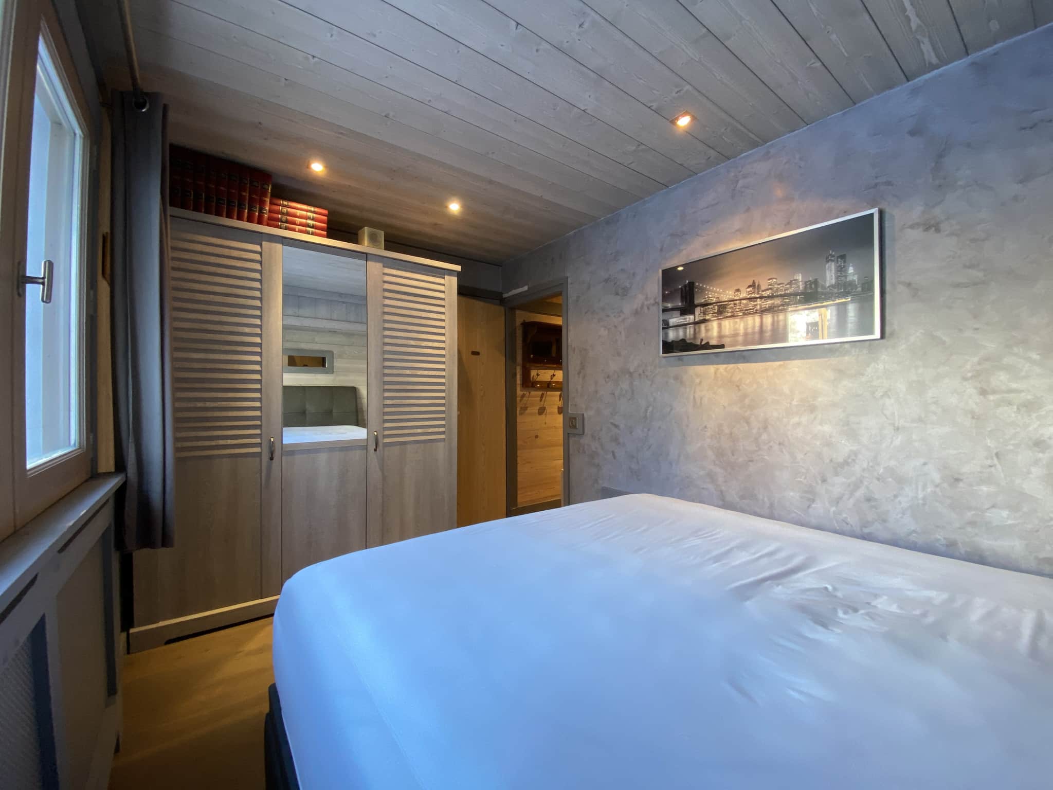 Bedroom in a renovated apartment with bed and wardrobe, waxed concrete walls, soft lighting.