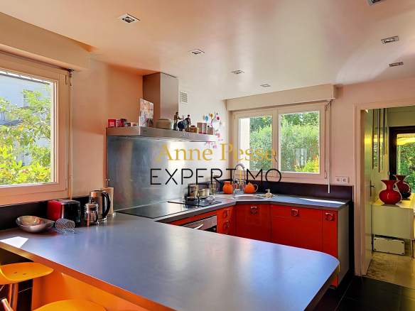 Cuisine moderne avec îlot central et fenêtres donnant sur un jardin, dans une villa d'architecte à Saint-Maur-des-Fossés.
