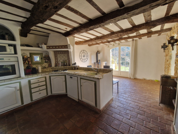 Intérieur d'une cuisine provençale avec poutres apparentes et carrelage en terre cuite.