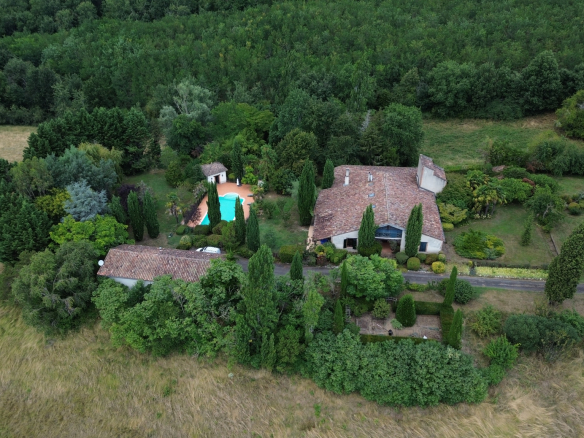 Vue aérienne d'une maison de campagne avec piscine et maison d'amis, entourée de jardins verdoyants.