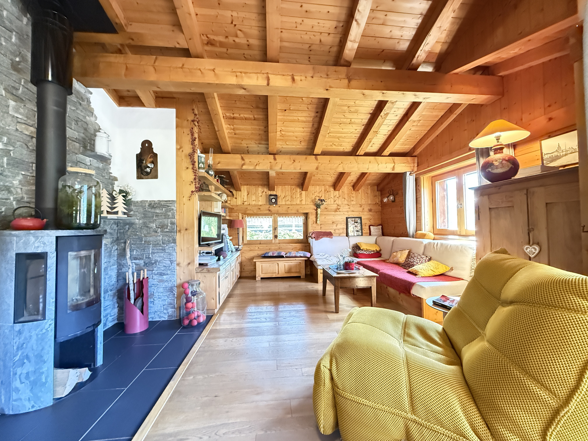Interior of a traditional chalet with a wooden living room, wood-burning stove and comfortable sofa.